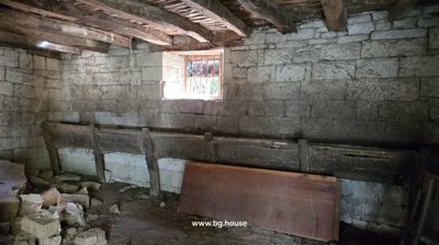 Interior view of the stone cellar showing wooden beams and a small barred window.