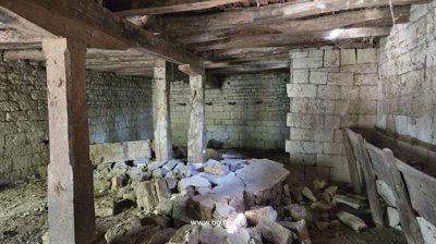 Stone cellar featuring wooden support pillars and rubble scattered on the floor.
