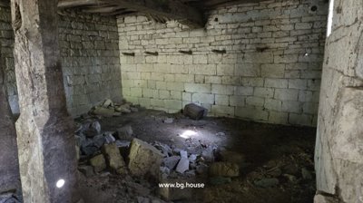 View of a stone cellar room with rubble on the floor and wooden beams overhead.