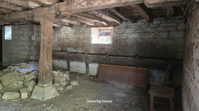 Interior view of a stone cellar showing wooden support beams, rubble on the ground, and stone walls with small windows.