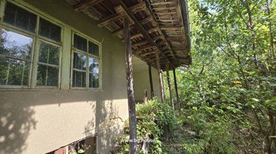 Traditional Bulgarian house exterior showing wooden roof supports and surrounding greenery.