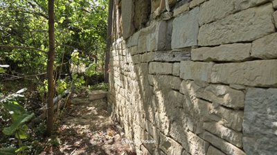 Side view of a stone wall exterior surrounded by dense green foliage and tree shadows.