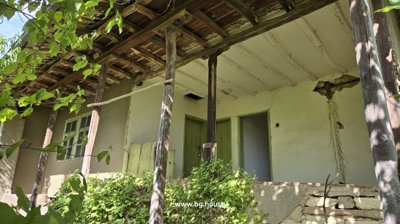 Wooden balcony supported by wooden posts with green doors and white plaster walls behind.