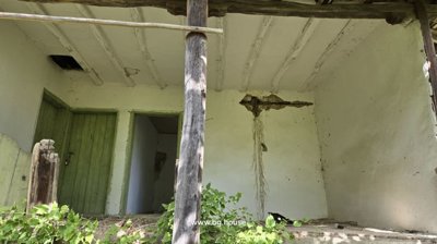 Porch area showing wooden beams supporting the roof and green doors with wall damage.