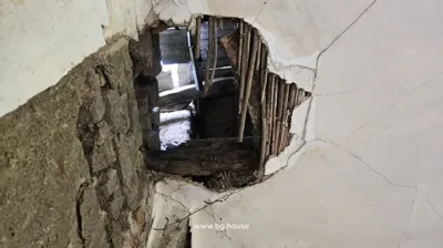 Interior view of a ceiling with a large hole exposing wooden beams and plaster damage