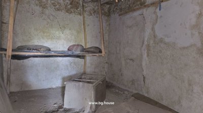 A small rustic room with rough plaster walls, a suspended wooden frame holding cushions, and a concrete square structure in the middle.