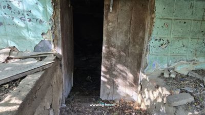 View through a wooden door into a dark interior room with blue-green painted walls and scattered debris on the floor.