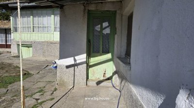 Green painted door entrance to a white plastered building with concrete pathway and window with lace curtains.