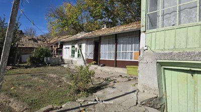 Side view of a village house showing enclosed veranda with green windows and concrete steps leading to the entrance.
