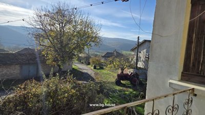 View from a balcony showing a village street, trees, houses, and a red tractor parked nearby.