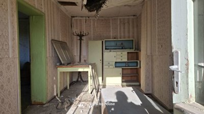 Interior room showing patterned wallpaper, green door and window frames, wooden furniture, and a damaged ceiling area.