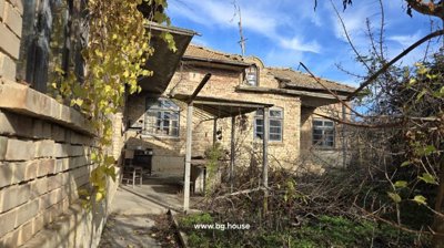 View of the brick house exterior featuring a tiled roof and a covered porch with outdoor furniture and dry vegetation