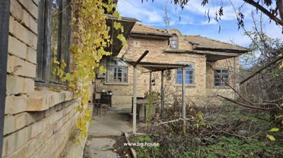 Exterior view of the brick house showing windows, a covered porch, and dry vines growing nearby