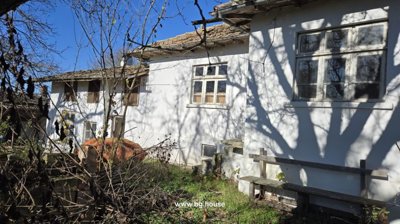 Side facade of the white cottage showing several windows and a wooden bench beside an overgrown garden area.