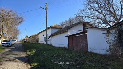 View along the village street showing the white cottage, adjacent outbuildings, parked cars, and a utility pole.