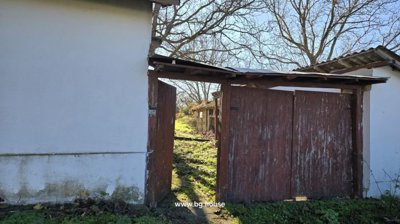 Open wooden gate in the white wall providing access to the garden area with trees and outbuildings behind.