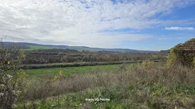 Garden area with bushes leading to open fields and distant hills under a cloudy sky