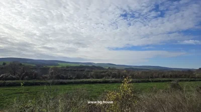 Panoramic view of green fields, trees, and distant hills under a partly cloudy sky