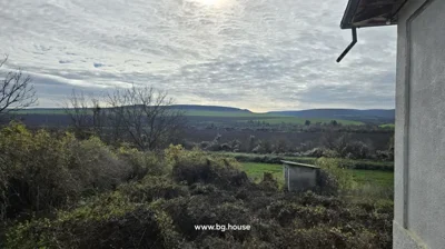 Garden area with bushes and trees, looking out towards distant hills under a cloudy sky