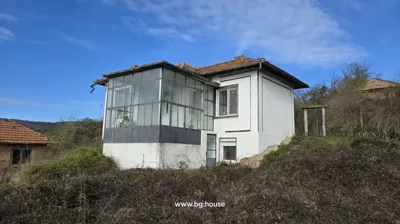 View of a white two-storey house with a glass porch and tiled roof from the garden area