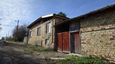 Exterior view of a brick house with a red wooden gate and two dogs on the dirt road beside it.