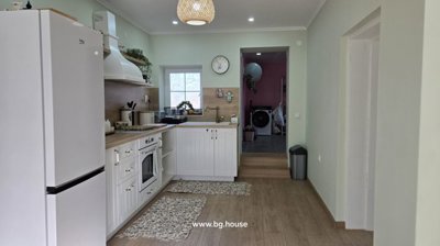 Interior of a kitchen showing white cabinets, an oven, a sink under a window, and decorative items on shelves.