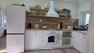 Corner of kitchen featuring white cabinets, oven, refrigerator, and wooden open shelves with kitchen items.