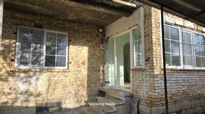 Corner of the brick house showing large windows and concrete steps leading up to a glass door entrance.