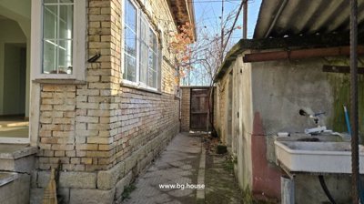 Narrow paved path running alongside the brick house featuring an outdoor sink and a wooden gate at the end.