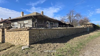 Stone wall enclosing a traditional Bulgarian house with tiled roof and chimney under clear blue sky