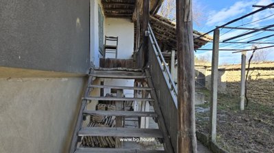 Wooden stairs with railing leading to an upper floor balcony with wooden posts and a chair visible