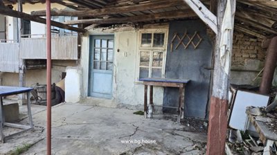 Covered porch area featuring a blue door, window, wooden table, and rustic wall
