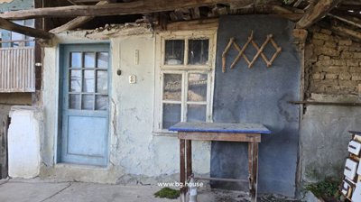 Covered porch area with a blue door, window, wooden table, and rustic wall