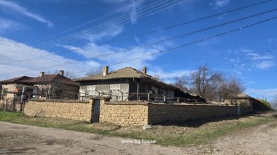 Corner perspective showing stone wall surrounding a Bulgarian house with tiled roof and dirt road