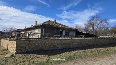 Side of Bulgarian house showing wooden balcony and stone wall under blue sky