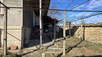 Open wooden gate in stone wall showing stairs and yard area of house