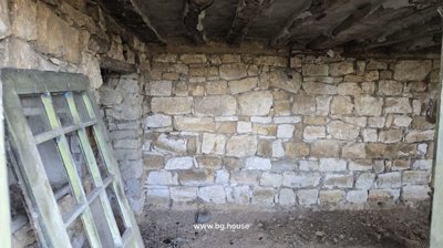 Interior view showing a rough stone wall with a green-painted wooden window frame leaning against it.