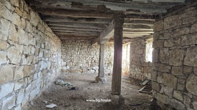 Room inside the house featuring stone walls, exposed wooden ceiling beams, and a dirt floor.