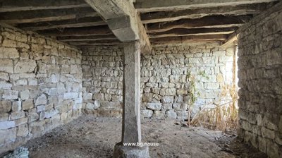 Interior stone room illuminated by natural light through window openings, showing rough stone walls and dirt floor.