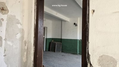 Interior view of a room showing peeling white and green walls, wooden floor, and old window frames