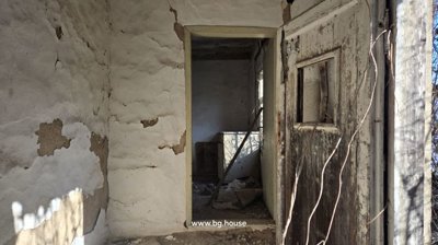 Interior view showing peeling plaster on walls and an old wooden door with a small window opening.