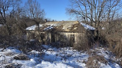An old house with a partially damaged roof and snow on the ground, surrounded by bare trees in winter.