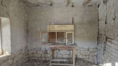 An empty interior room showing rough plaster walls, wooden beams, and natural light from a window.