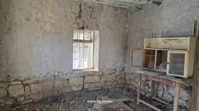 An interior room with rough stone and plaster walls, a window, and a doorway leading to another room.