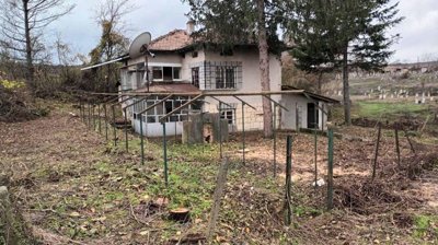 View of the two-storey house with a tiled roof, enclosed porch, and garden space with trees and fencing