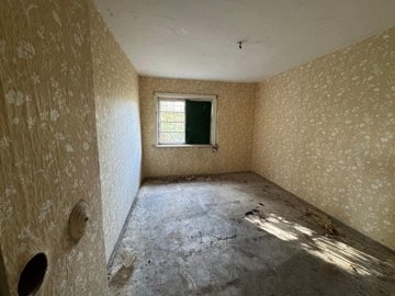An empty room featuring beige floral wallpaper and a small window partially covered with a green board.