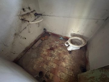 A small bathroom showing an old toilet and a wall-mounted basin frame without the basin.