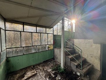 Covered entrance showing stairs, green metal panels, and barred windows with sunlight