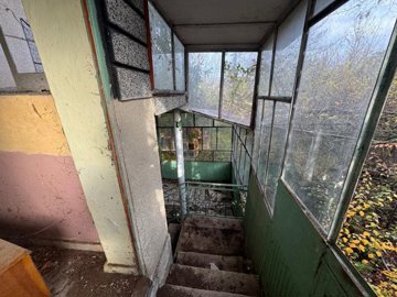 Enclosed porch area featuring stairs leading down, green metal panels, and barred windows