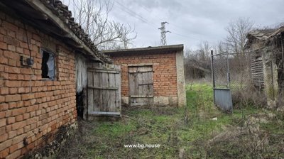 Brick outbuildings featuring wooden doors and a metal gate in a grassy yard area.